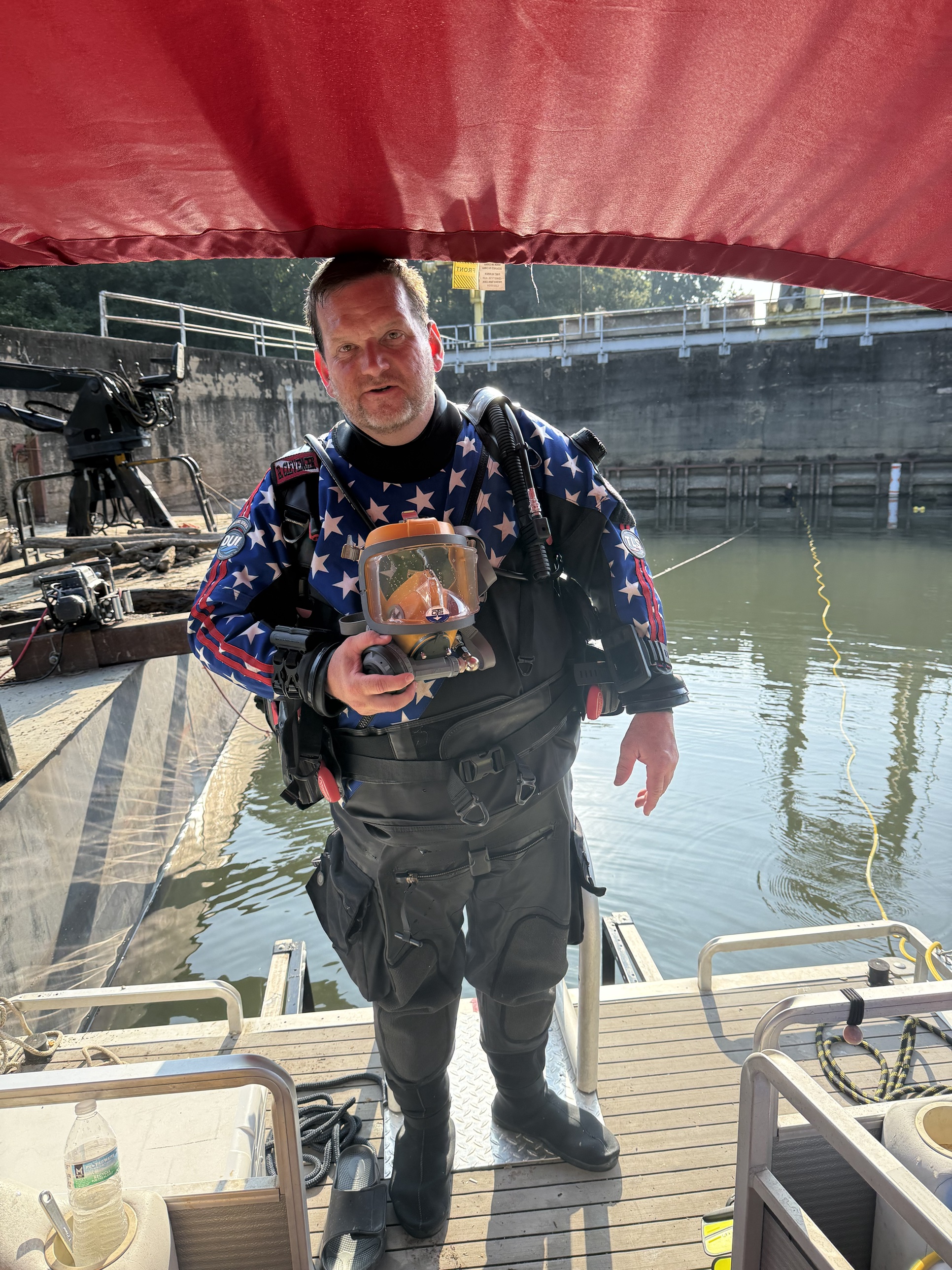 Brent Clevenger of Sink or Swim Scuba in a DUI drysuit holding an orange Interspiro Divator (AGA) full-face mask on the dive barge at Turner Shoals Dam, Lake Adger, NC